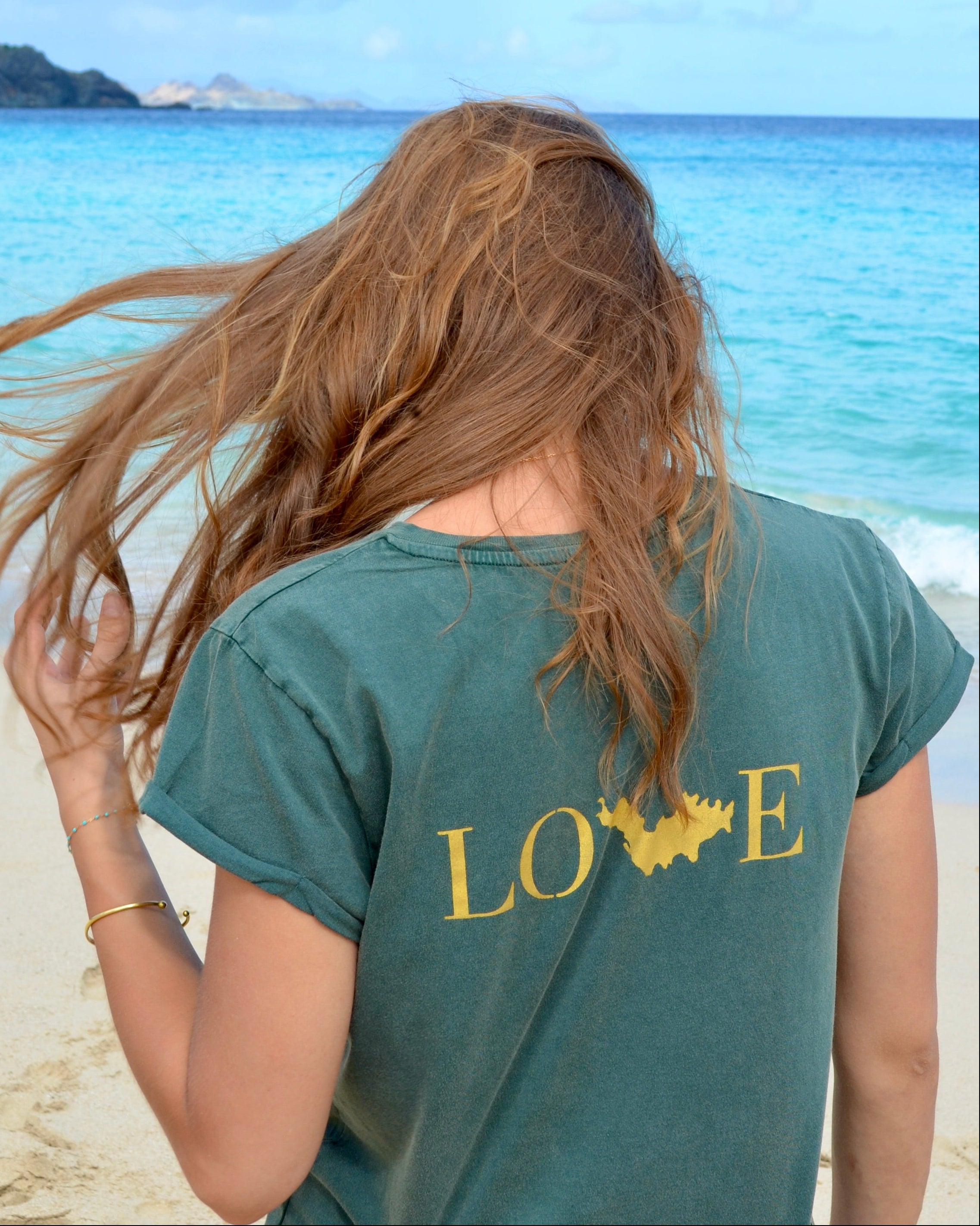 Hannah porte un T-shirt kaki avec le visuel Love doré, sur la plage